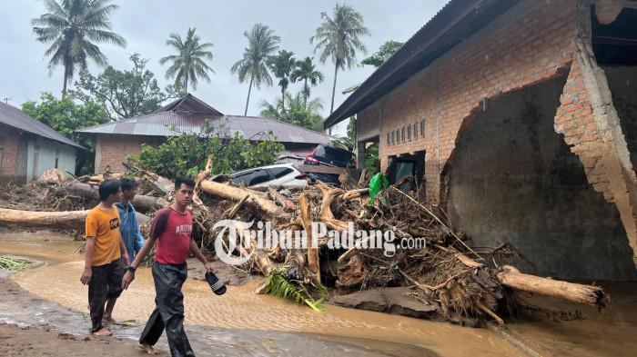 BANJIR BANDANG- Beberapa warga melintas di lokasi banjir bandang yang mengakibatkan rumah rusak, mobil hanyut, dan air membawa material berupa batang pohon di kawasan perumahan Lumin Park Cluster, Kecamatan Koto Tangah, Kota Padang, Sumatera Barat, Kamis (27/11/2025).
