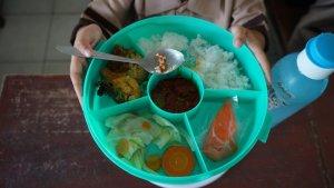 Siswa-menunjukan-menu-MBG-yang-sedang-ia-santap.jpg
