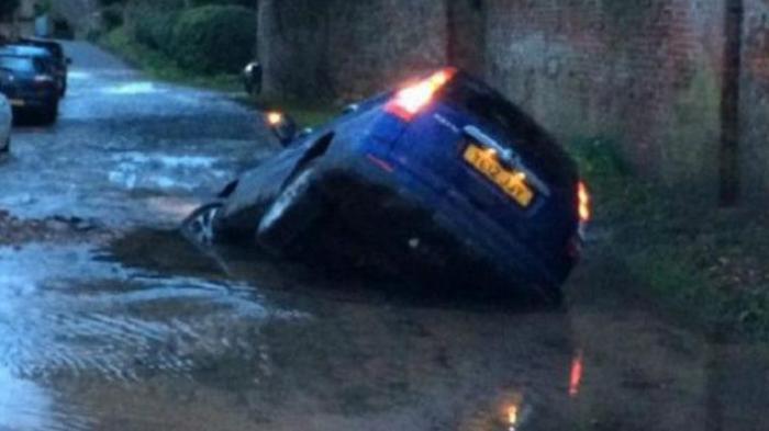 Pipa Air di Badan Jalan Pecah, Sebuah Mobil Tersedot ke dalam Lubang
