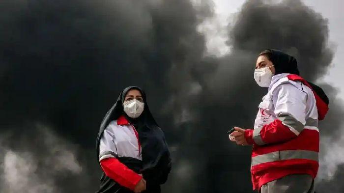 Dua-anggota-Bulan-Sabit-Merah-Iran-berdiri-saat-kepulan-asap-dari-pemboman-kilang-minyak-Shahran.jpg