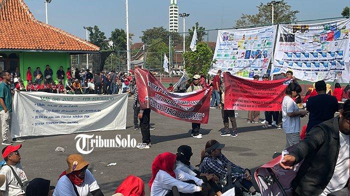 SUARAKAN TUNTUTAN - Buruh yang tergabung dalam Forum Peduli Buruh Sukoharjo membentangkan sepanduk yang bertuliskan tuntutan dan harapan di hari buruh internasional 2025 di GOR Jombor Sukoharjo, Kamis (1/5/2025). Tidak melalui aksi turun ke jalan, aliansi buruh ini memilih cara berbeda dengan menggelar senam bersama dan hiburan musik di GOR Jombor Sukoharjo.