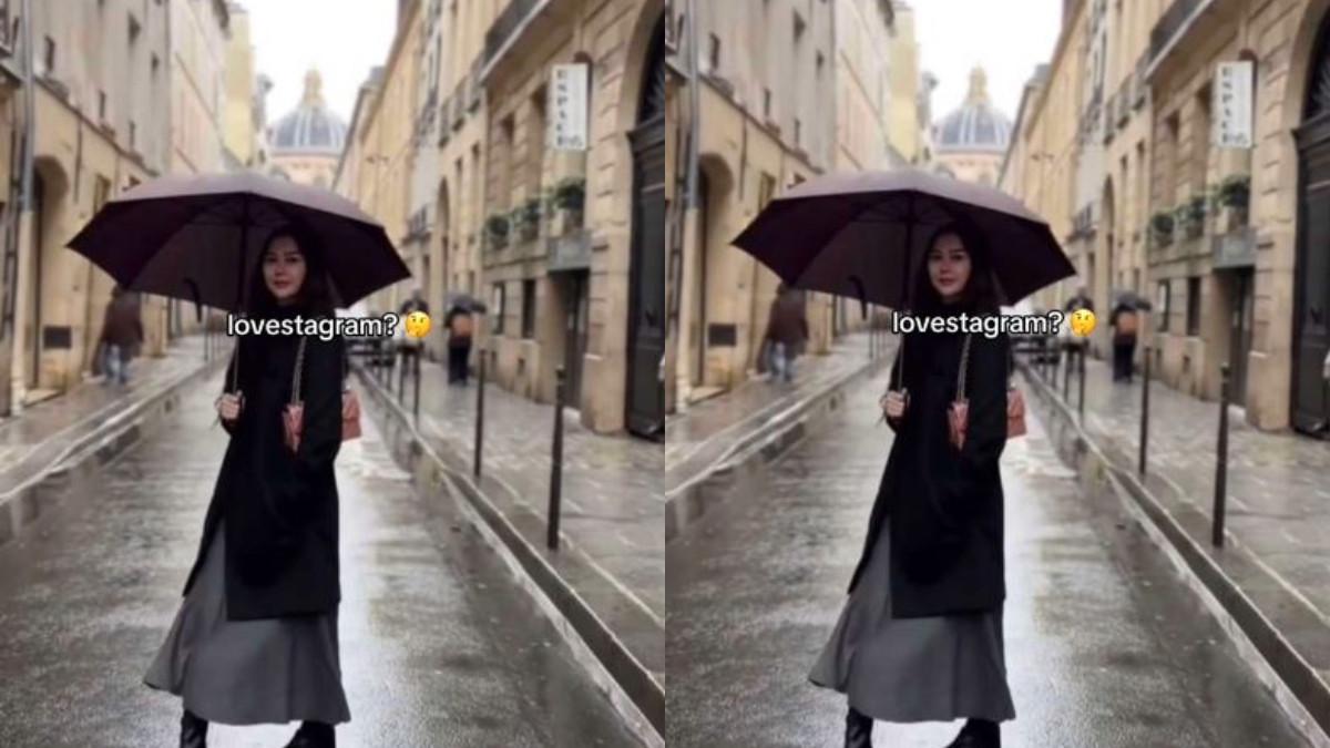 Aura Kasih terlihat memegang payung dengan tulisan kecil di pojok foto bertuliskan 