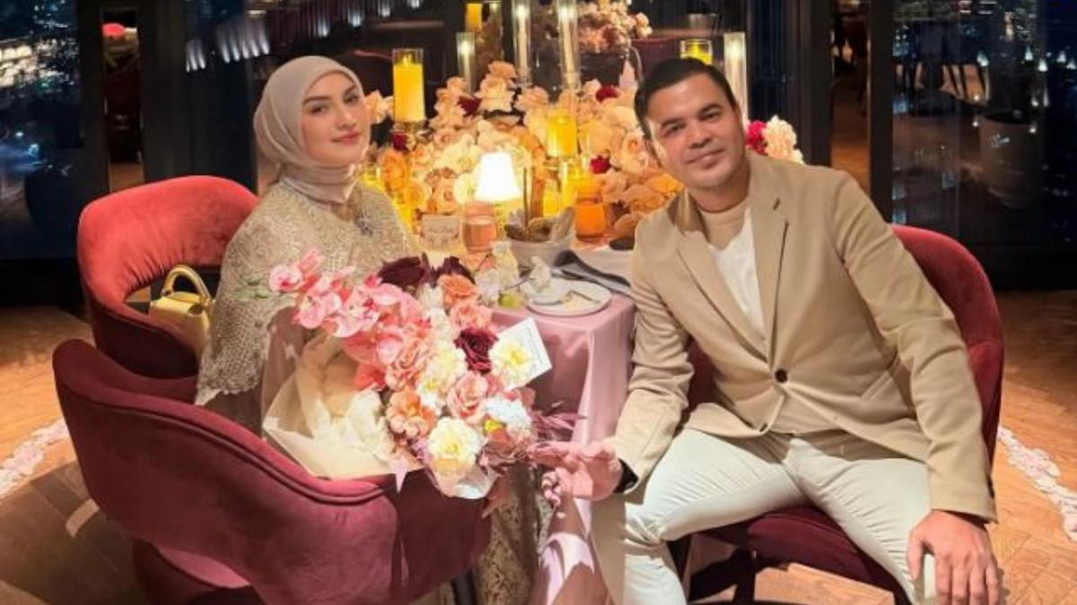 PERAYAAN ANNIVERSARY - Meja mereka dihias cantik dengan bunga berwarna pastel, lilin berkelip lembut, dan kelopak bunga berbentuk hati di permukaannya.