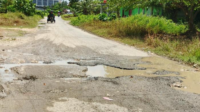 JALAN RUSAK-Kondisi jalan menuju Pasar Smart Pasangkayu yang rusak parah dengan lubang dan genangan air, Kamis (18/9/2025). Warga berharap pemerintah segera melakukan perbaikan, namun rencana tersebut tertunda akibat pemangkasan anggaran Rp18 miliar.