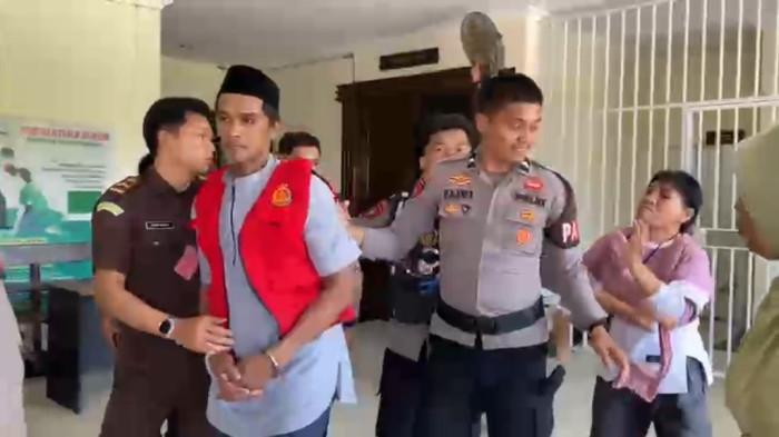 SIDANG KASUS PEMBUNUHAN - Terdakwa kasus pembunuhan karyawati koperasi, Hijrah, dikawal ketat aparat kepolisian usai sidang di Pengadilan Negeri Pasangkayu, Selasa (28/4/2026). Suasana sempat memanas saat keluarga korban berusaha mendekati terdakwa akibat penundaan sidang tuntutan.