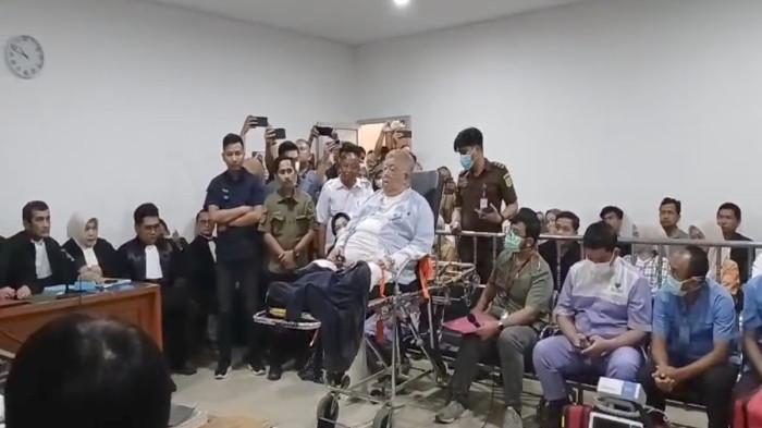 H HALIM -- Dengan duduk di kursi pasien dan didampingi tim medis, Dirut OT Sentosa Mulia Bahagia, Kms H Abdul Halim tiba di Museum Tekstil Palembang untuk menjalani sidang perdana kasus dugaan korupsi pemalsuan dokumen tol Betung-Tempino, Kamis (4/12/2025). Di ruang sidang H Abdul Halim Ali terbaring dengan tabung oksigen.