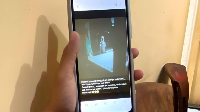 VIRAL TEROR POCONG - Seorang warga Bondowoso melihat foto viral pocong yang masih belum diketahui apakah editan AI atau bukan. Masyarakat di Desa Sumber Tengah, Kecamatan Binakal, Bondowoso, Jawa Timur, heboh dengan beredarnya foto pocong yang bersamaan muncul aksi gedor pintu rumah warga oleh sosok misterius saat dini hari pada Minggu (24/5/2026).