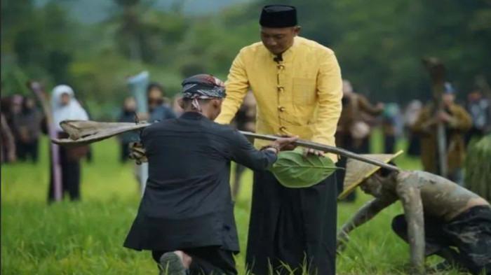 BONGKOK BOLONG  - Bupati Pacitan Indrata Nur Bayuaji sebagai pemimpin ritual Thetek Melek menyerahkan 'Bongkok Bolong' pada mbah Lurah (Lurah Setempat) di hamparan sawah di Desa Sukoharjo, Kecamatan/Kabupaten Pacitan, Jatim, Minggu (21/12/2025). Ritual adat Thetek Melek yang digelar setahun sekali ini mempertemukan warga, seniman, dan pemimpin daerah dalam satu prosesi sakral.