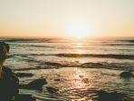Ilustrasi-pantai-dengan-pemandangan-sunset-yang-terlihat-di-antara-dua-tebing.jpg