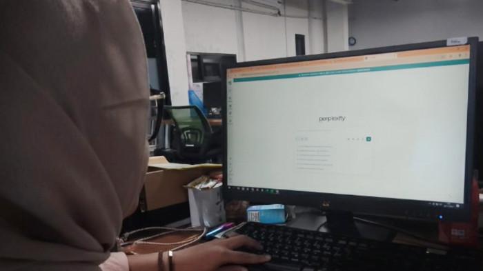 GUNAKAN AI - Adhila Paramitha Larasati, mahasiswa jurusan Manajemen Administrasi Universitas Sebelas Maret Surakarta (UNS) saat menggunakan sebuah platform AI pada komputer yang digunakannya, Kamis (27/11/2025).