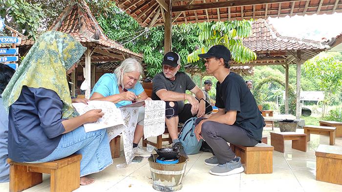 BELAJAR MEMBATIK - Giyanti (kiri), pembatik di Desa Wisata Wukirsari sedang memandu Jiel (tengah) - wisatawan asing asal Kanada - membatik, di Gazebo Kampung Batik Giriloyo, Wukirsari, Imogiri, Bantul, Senin (20/10/2025).