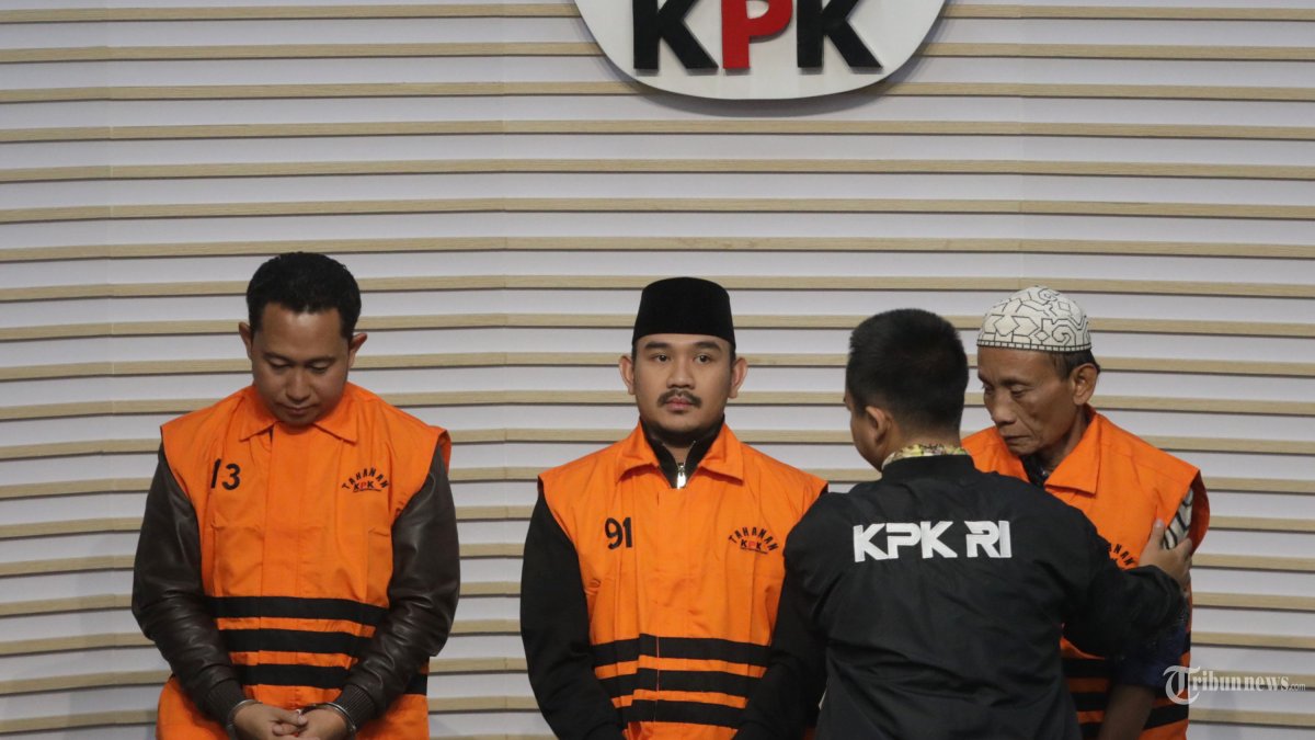 OTT KPK - Bupati Kabupaten Bekasi Ade Kuswara Kunang (tengah) bersama  Kepala Desa Sukadami, Kecamatan Cikarang Selatan M Kunang (kanan) dan Pihak Swasta Sarjan mengenakan rompi tahanan usai terjaring operasi tangkap tangan (OTT) di Gedung Merah Putih KPK, Jakarta, Sabtu (20/12/2025).