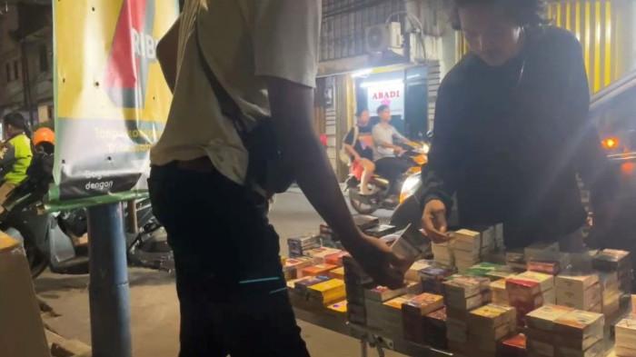 ROKOK ILEGAL – Pedagang rokok ilegal menjajakan sejumlah bungkus rokok dagangannya di kawasan Jakarta Barat, Selasa (14/10/2025). Lapak terbuka ini menjadi bagian dari sistem distribusi yang disebut pedagang menghasilkan untung hingga Rp60 juta per bulan, dengan dugaan setoran ke oknum aparat untuk menghindari razia.