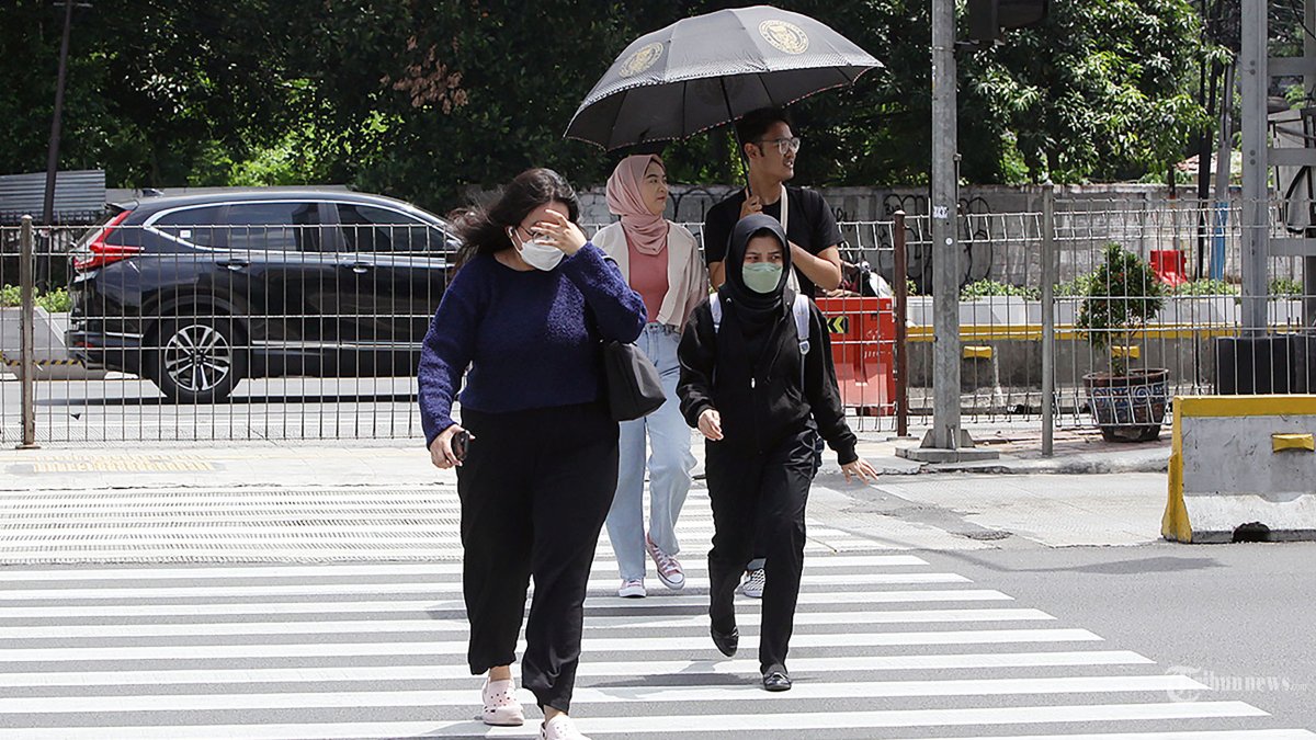 Pekerja melindungi tubuh dari terik matahari menggunakan payung saat berjalan di kawasan Sudirman, Jakarta, Kamis (21/12/2023).