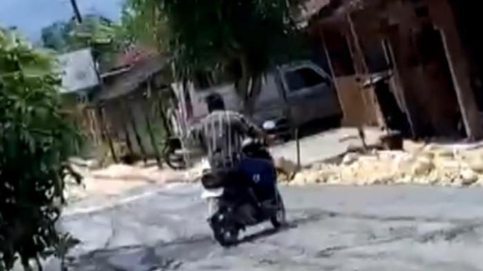 RUSAK JALAN COR - Warga Palon, Agus Sutrisno, saat melintasi jalan cor yang kondisinya masih basah, Jumat (20/2/2026).