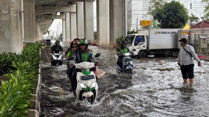 PERJUANGAN OJOL – Seorang pengemudi ojek online (ojol) melintasi genangan air di Jalan Boulevard Baru Raya, Kelapa Gading, Jakarta Utara, Minggu (18/1/2026). Meski argo tipis dan risiko tinggi, mereka tetap berusaha menyelesaikan pesanan.