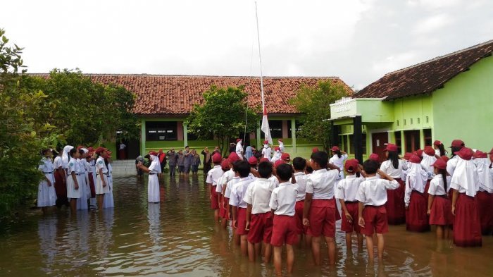 Siswa-siswi SD Negeri Sayung 1, Kabupaten Demak, tetap menjalankan upacara bendera Merah Putih meski sekolah mereka masih terendam banjir pada Senin (13/2/2017)