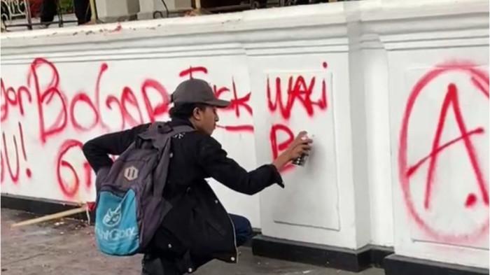 VANDALISME - Salah satu pengunjuk rasa terlihat mencorat-coret tembok Kantor Balai Kota Bogor saat demo berlangsung, Kamis (21/8/2025).