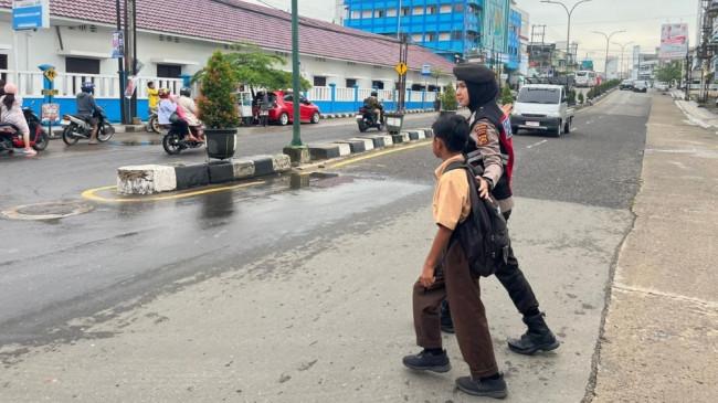Personel Polda Jambi Bantu Anak Sekolah Seberang Jalan saat Lalu Lintas Padat di Pagi Hari