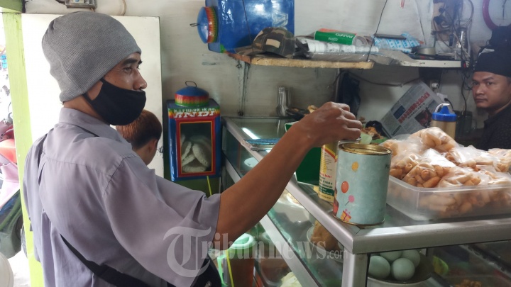 Warga Memasukan Sumbangan Uang Dikotak Amal di Warung