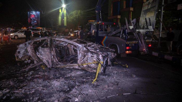 Orang-orang berdiri di samping kendaraan yang dibakar di luar Stadion Kanjuruhan di Malang, Jawa Timur, pada 2 Oktober 2022. Setidaknya 127 orang tewas di sebuah stadion sepak bola di Indonesia ketika suporter menyerbu lapangan dan polisi merespons dengan gas air mata, yang memicu penyerbuan. kata pihak berwenang pada 2 Oktober