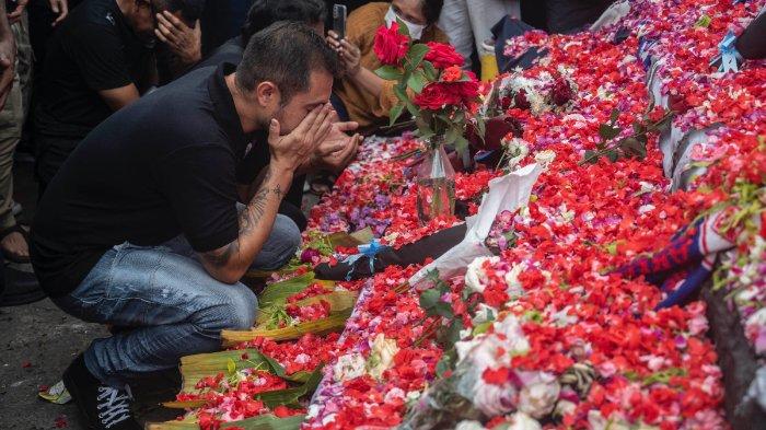 Para pemain dan ofisial Klub Sepak Bola Arema berkumpul untuk berdoa di samping bunga pada peringatan korban terinjak-injak di Stadion Kanjuruhan di Malang, Jawa Timur pada 3 Oktober 2022. Kemarahan terhadap polisi memuncak di Indonesia pada 3 Oktober setelah setidaknya 125 orang dikepung. tewas dalam salah satu bencana paling mematikan dalam sejarah sepak bola, ketika petugas menembakkan gas air mata di stadion yang penuh sesak, sehingga memicu keributan.