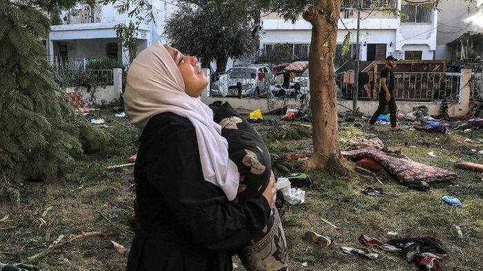 Seorang wanita bereaksi sambil memegang bantal saat dia berdiri di tengah puing-puing di luar lokasi rumah sakit Ahli Arab di Gaza tengah pada 18 Oktober 2023 setelah ledakan semalam di sana. Sebuah ledakan melanda sebuah rumah sakit di Gaza yang dilanda perang dan menewaskan ratusan orang pada tanggal 17 Oktober malam, memicu kecaman global dan protes kemarahan di seluruh dunia Muslim. Juru bicara militer Israel pada tanggal 18 Oktober mengatakan bahwa Israel memiliki 