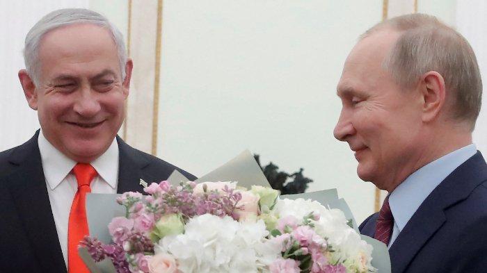 Presiden Rusia Vladimir Putin memegang bunga di samping Perdana Menteri Israel Benjamin Netanyahu saat mereka bertemu di Kremlin di Moskow pada 30 Januari 2020.