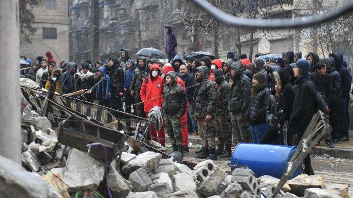 Penonton menyaksikan tim penyelamat mencari korban selamat di bawah reruntuhan bangunan yang runtuh di kota Aleppo, Suriah utara.
