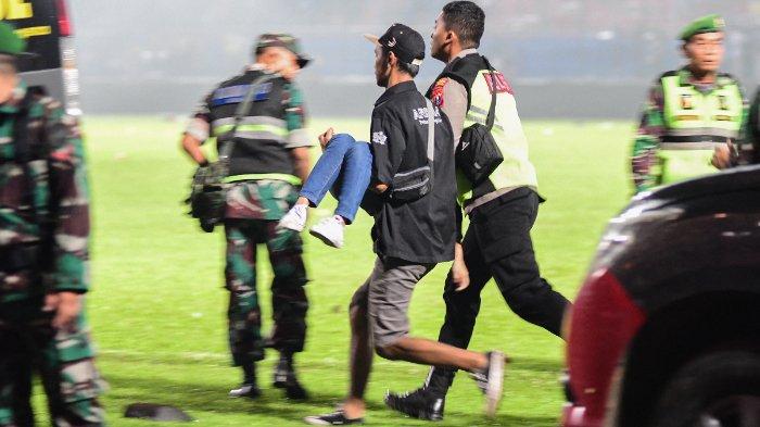 Gambar yang diambil pada 1 Oktober 2022 ini memperlihatkan orang-orang berlarian bersama penonton yang terluka usai pertandingan sepak bola antara Arema FC dan Persebaya di Stadion Kanjuruhan Malang, Jawa Timur. Kemarahan terhadap polisi meningkat di Indonesia pada tanggal 3 Oktober setelah sedikitnya 125 orang tewas dalam salah satu bencana paling mematikan dalam sejarah sepak bola, ketika petugas menembakkan gas air mata di stadion yang penuh sesak, yang memicu terjadinya desak-desakan.